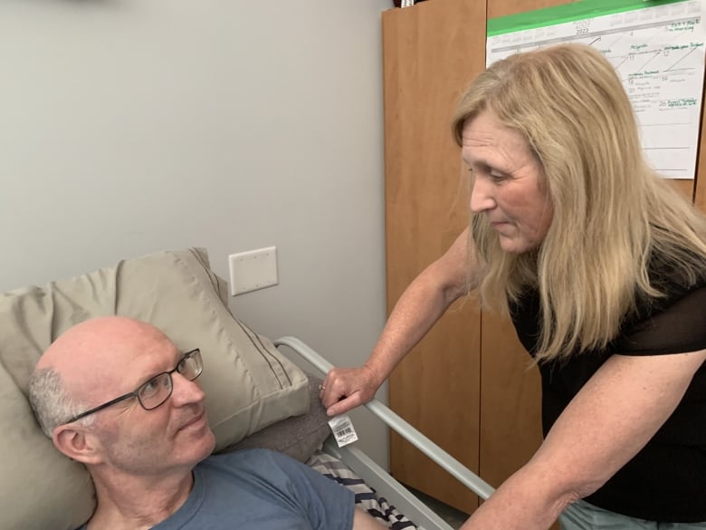 A man in a hospital-type bed looks up at a woman who is leaning over the edge of his bed.