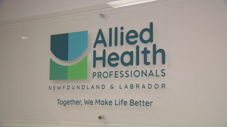 The logo of the Association of Allied Health Professionals of Newfoundland and Labrador hangs on a wall. Text underneath the logo reads 'Together, we make life better.'