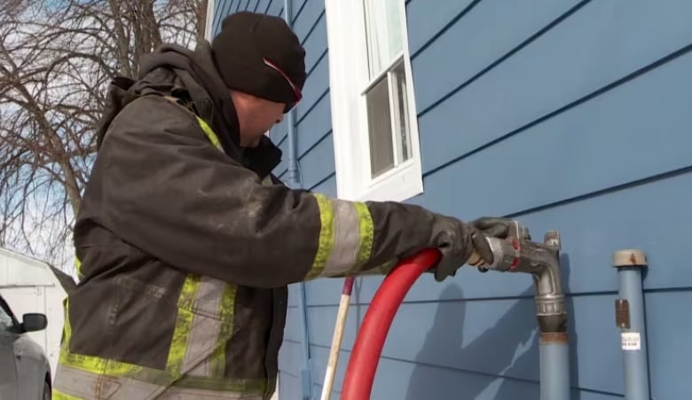 A worker fills a tank, attached to a house, with oil. 