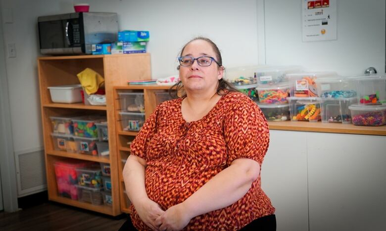 Woman in orange shirt looks off into distance at her daycare.