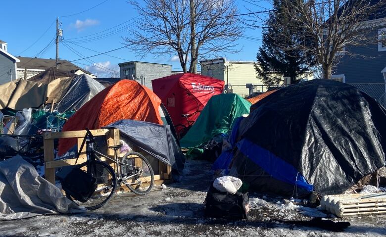 A group of tightly spaced and colourful tents and tarp enclosures with apartment buildings in the background. 