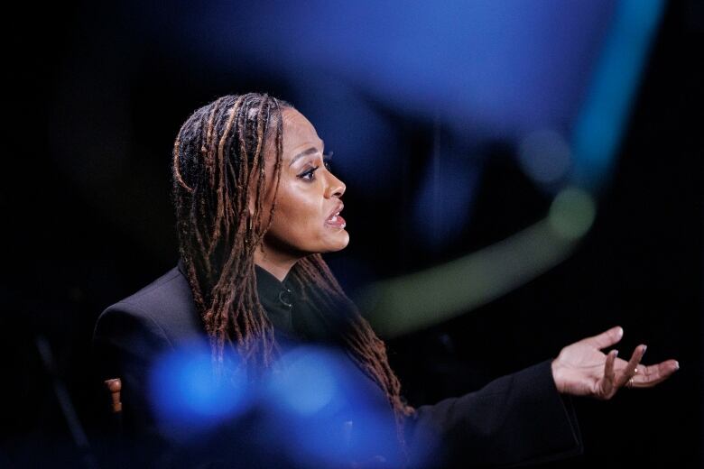 Filmmaker Ava DuVernay is shown in profile, gesturing with one hand outstretched