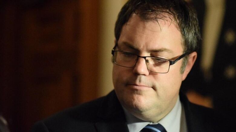 Man with dark brown hair wearing glasses wearing suit.