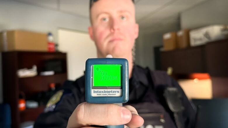 A police officer holds a device labelled Intoximeters which has a lit-up green screen.