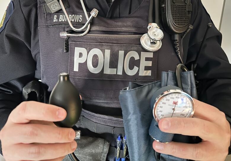 A police officer in uniform has a stethoscope around his neck and is holding a blood pressure monitoring cuff.