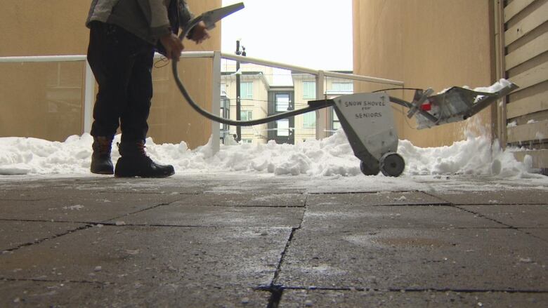 A metal cart-like device marked 'snow shovel for seniors' is pictured in a snowy balcony. The device scoops up snow on one end, with a man holding the other end by a handle.