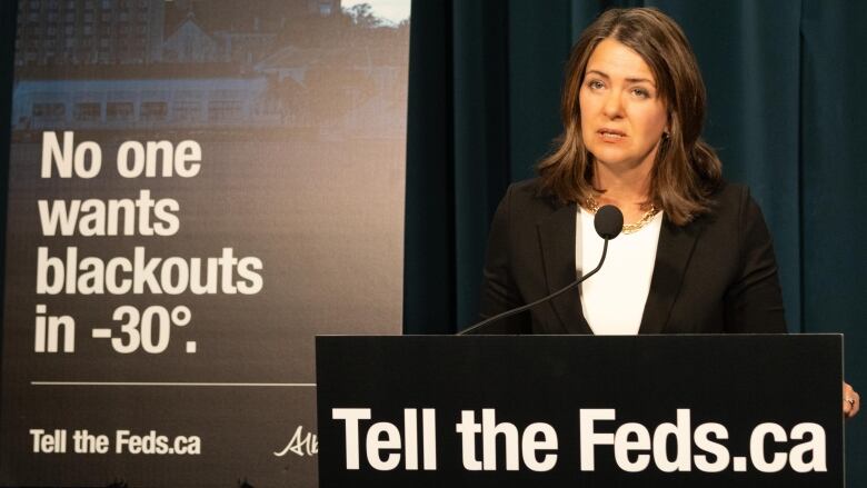 A politician stands at a podium beside campaign signs.