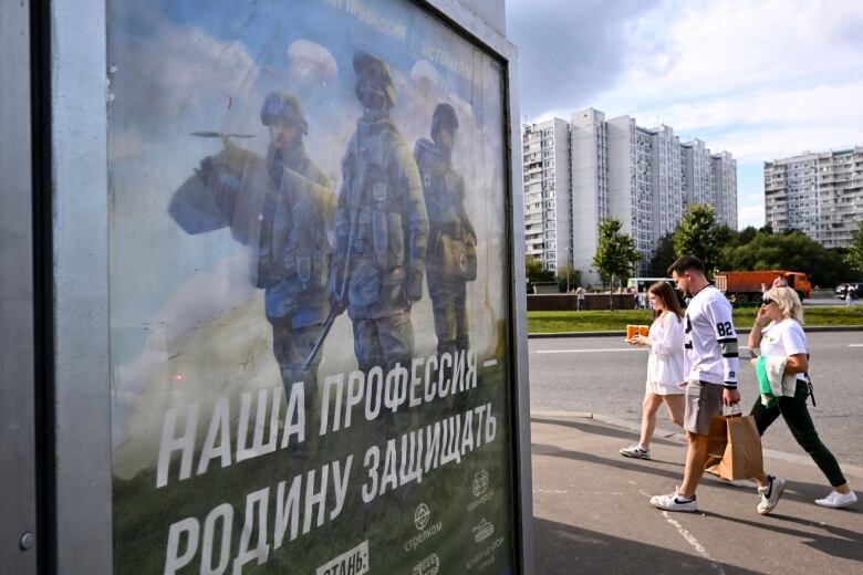 People in Moscow walk past a sign promoting contract service with the Russian military.