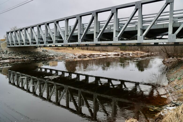 A side view of a metal bridge spanning a river/