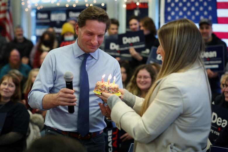 Woman gives man birthday cake as he's on a stage