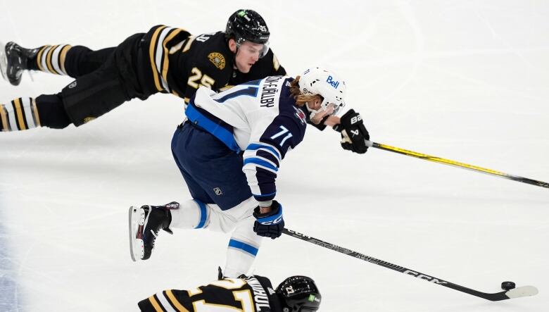 Two players chase for the puck while a third hockey player tries to catch up.