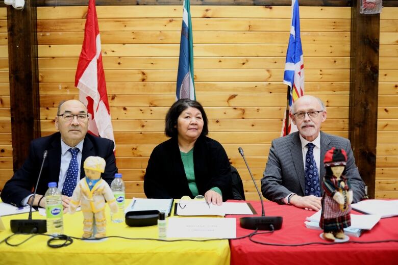 Two men and a woman seated at a table with microphones in front of them. 