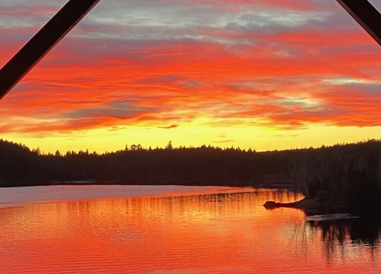 An orange and yellow sky is reflected in a body of water.