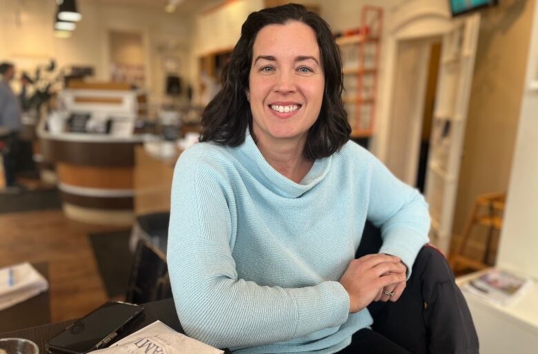 Woman with dark hair and blue sweater in a coffee shop. 