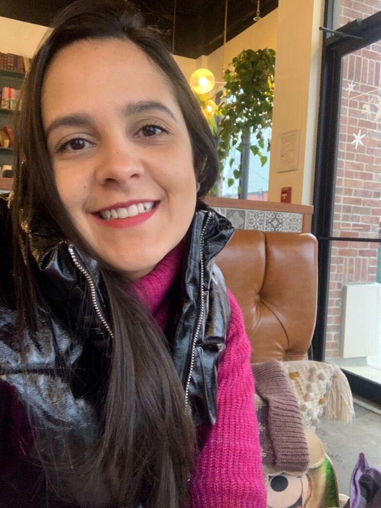 A young lady in a pink sweater sitting on a couch in a cafe.