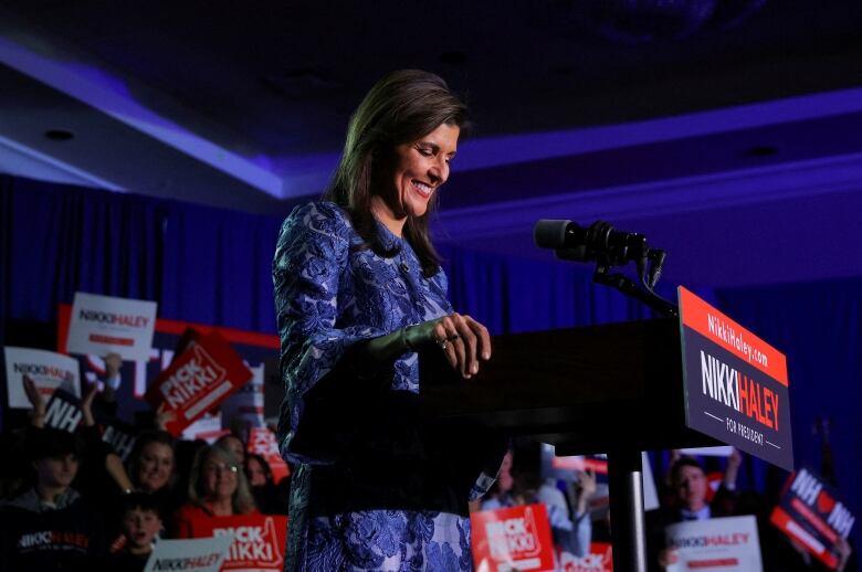 Haley smiles while staring down and clasping lectern, surrounded by white and red signs bearing her name