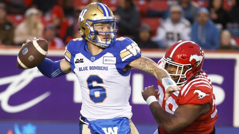 A football quarterback pulls his arm back to pass with an opponent chasing him.