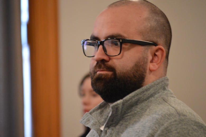 A man in glasses in a courtroom stares ahead