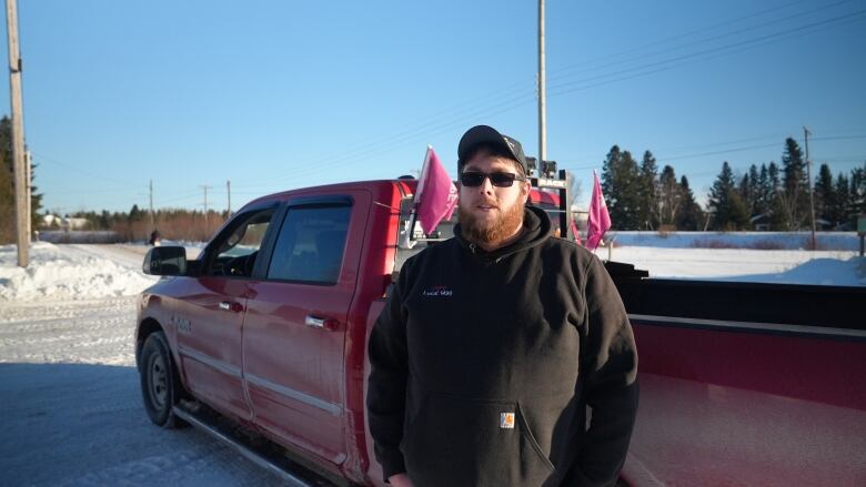 A man wearing sunglasses and a black hoodie, standing in front of a pickup truck.