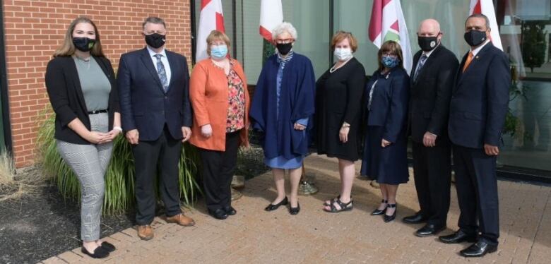 Eight people including a casually dressed student, three men in business suits, and four women in business clothing. All are masked as required by current COVID-19 protocols. 