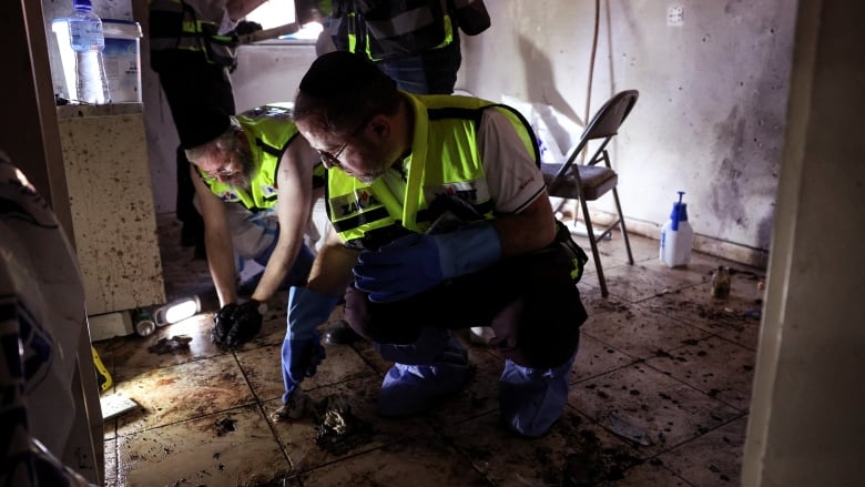 Men in high-viz vests collect evidence from the floor of a damaged house.