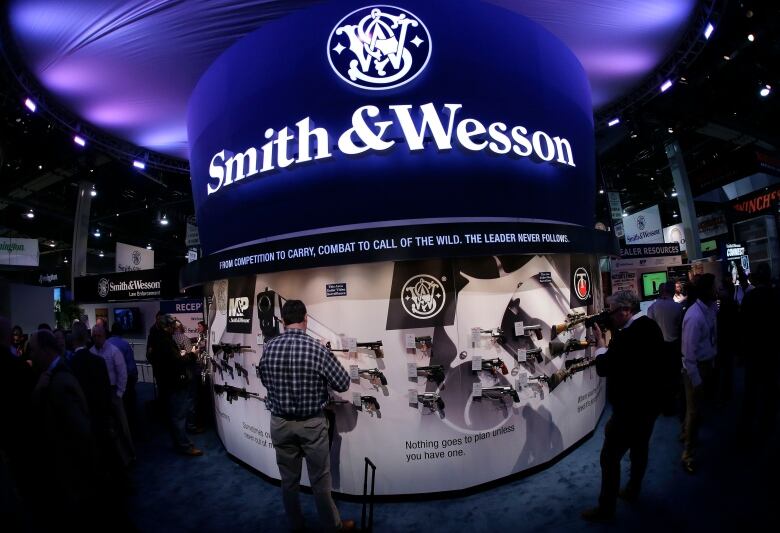 A number of people gather around a booth at a trade show marked 'Smith & Wesson'.