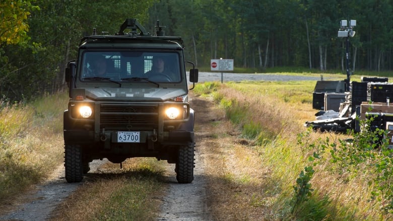 A green coloured Mercedes-Benz G-Wagon SUV drives along a hardpacked dirt road, next to a knee-high grassy field. 