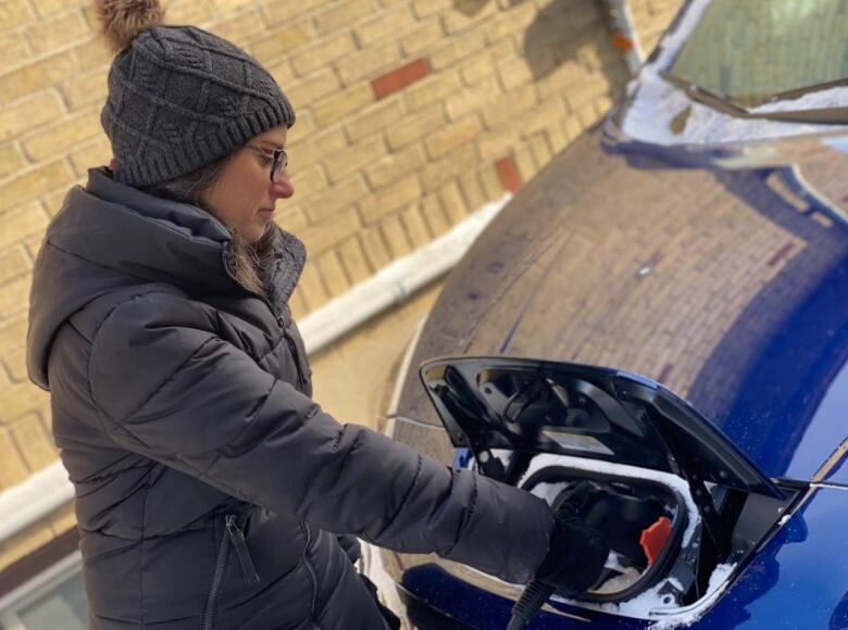 A woman plugs a charger into her electric vehicle.