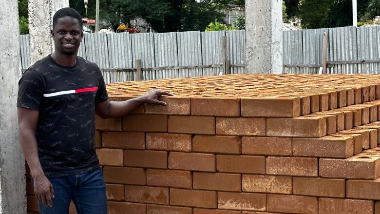 A person stands by a large stack of bricks. 