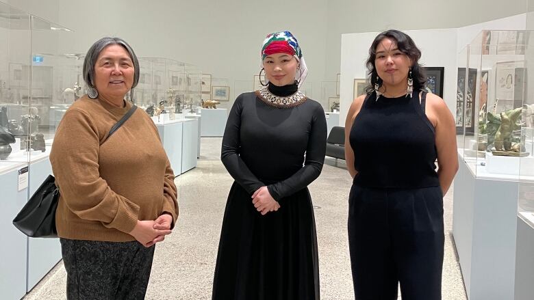 three Inuit women stand in an art gallery