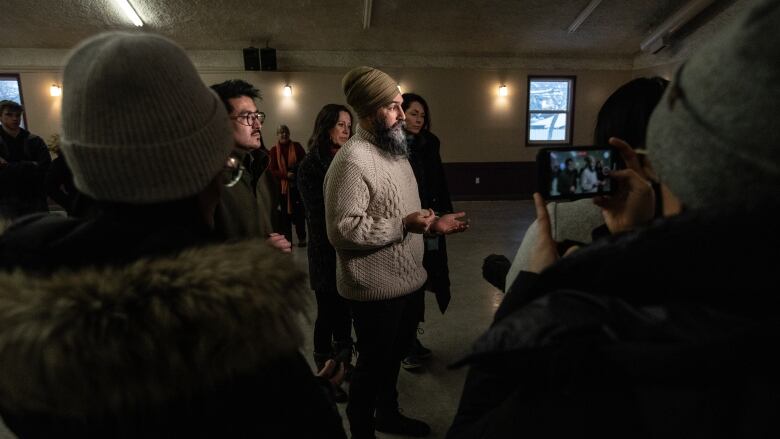 A man in a beige sweater speaks to reporters.