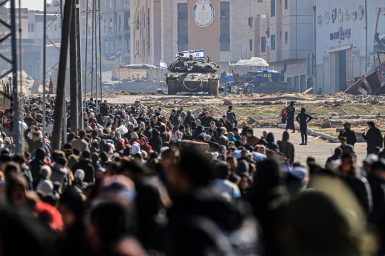 Masses of people are shown in the foreground, with a tank shown in the background.