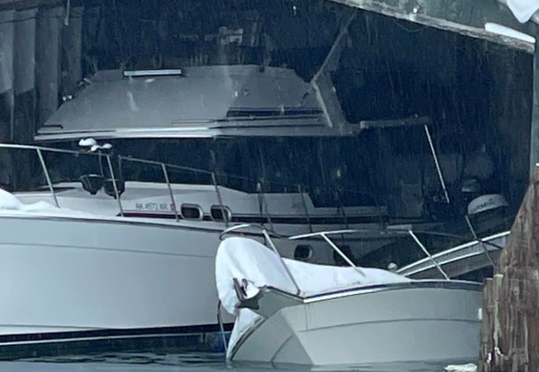 A boat tipped over and covered in snow next to a much larger boat that is still upright.