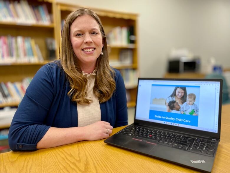 Jennifer Nangreaves poses next to a laptop, which shows the Early Childhood Development Association website. 