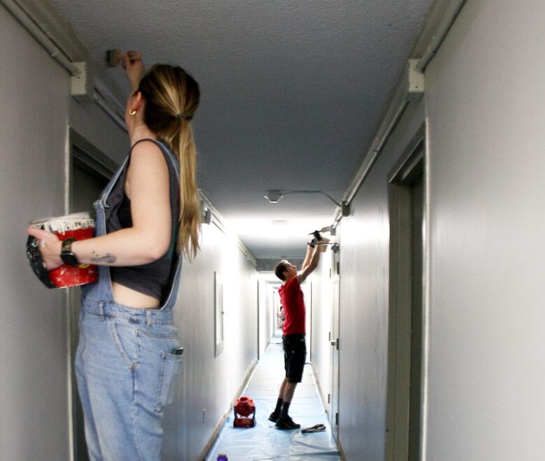 A woman stands on a ladder painting, and a man stands behind her also painting. 