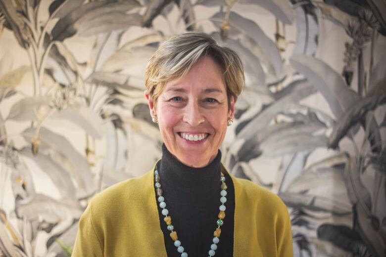 A headshot of a woman against a leafy wallpaper background. 