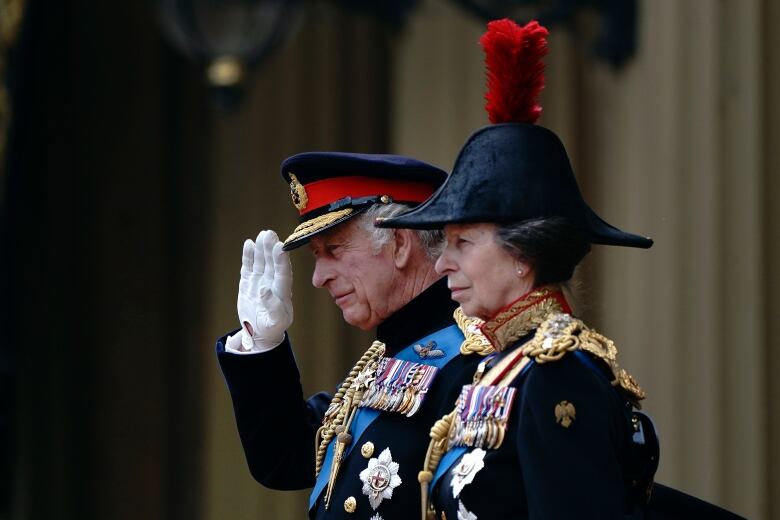 Two people wearing formal uniforms stand beside one another as one salutes.