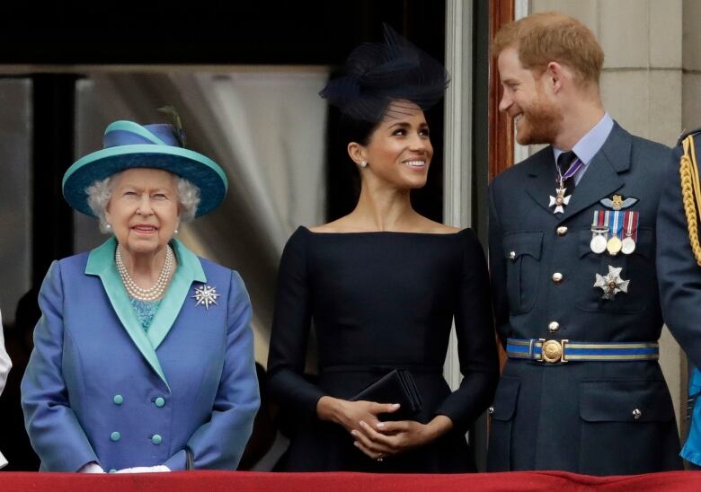 Three people stand on a balcony in front of an open door.