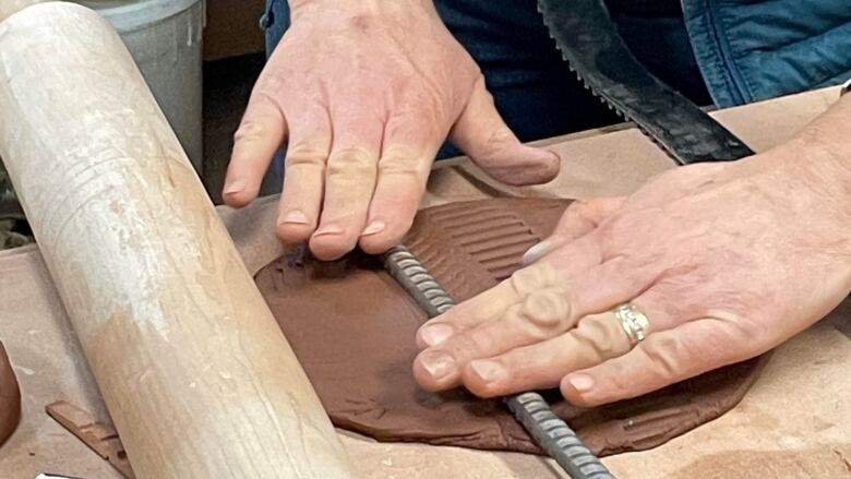 A shot of hands pressing down on a utensil in order to to do hand building pottery. 