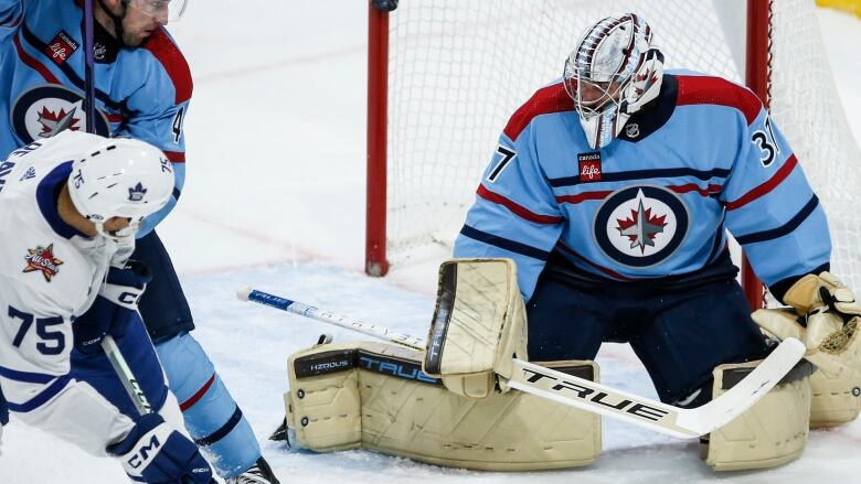 A battle in front of the goaltender by two hockey players.