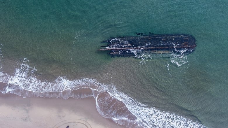 The dark, rotting hull of an old ship lies along the water's edge.