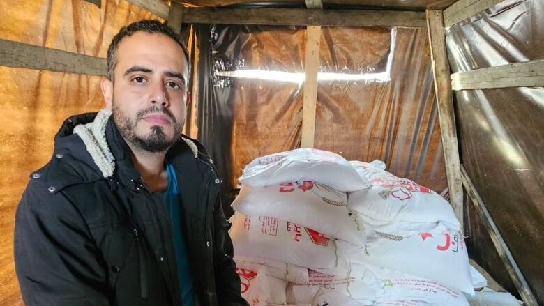 A man sits next to bags of wheat.