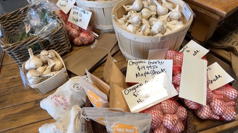 A wood table displays bulbs of garlic in mesh bags and baskets.