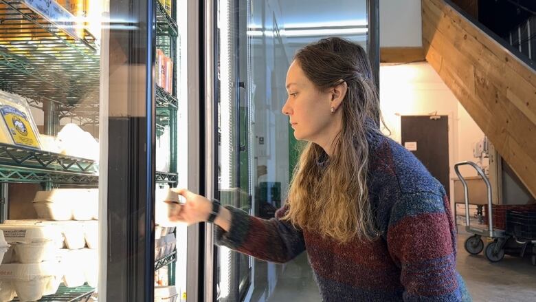 A woman stocks a commercial fridge in a warehouse market.