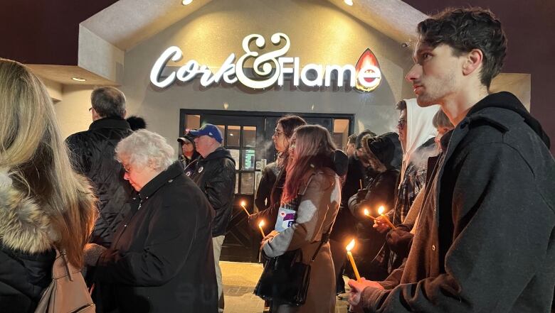 People with candles stand outside a restaurant.