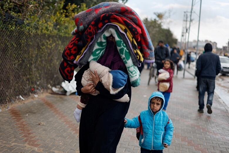 A woman carrying blankets atop her head holds hands with a small child while walking outdoors.