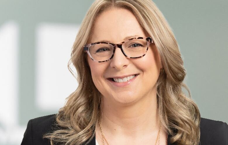 A woman with glasses and blond hair smiles at the camera.