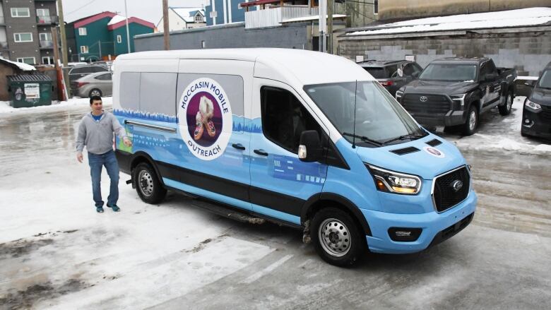 A large blue and white van on an icy street. A man is standing next to it.