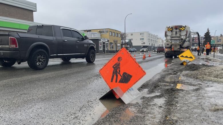 A road construction sign is seen on a wet, slushy city street.