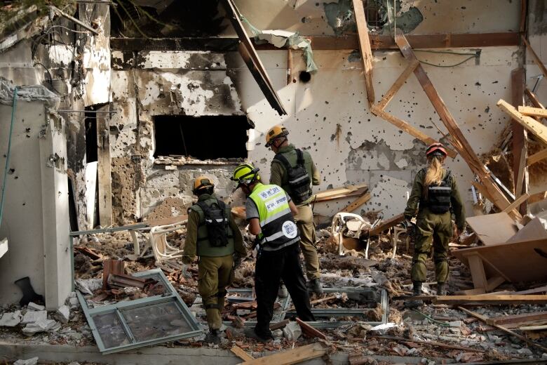 People wearing helmets and uniforms walk in the rubble of a home. 